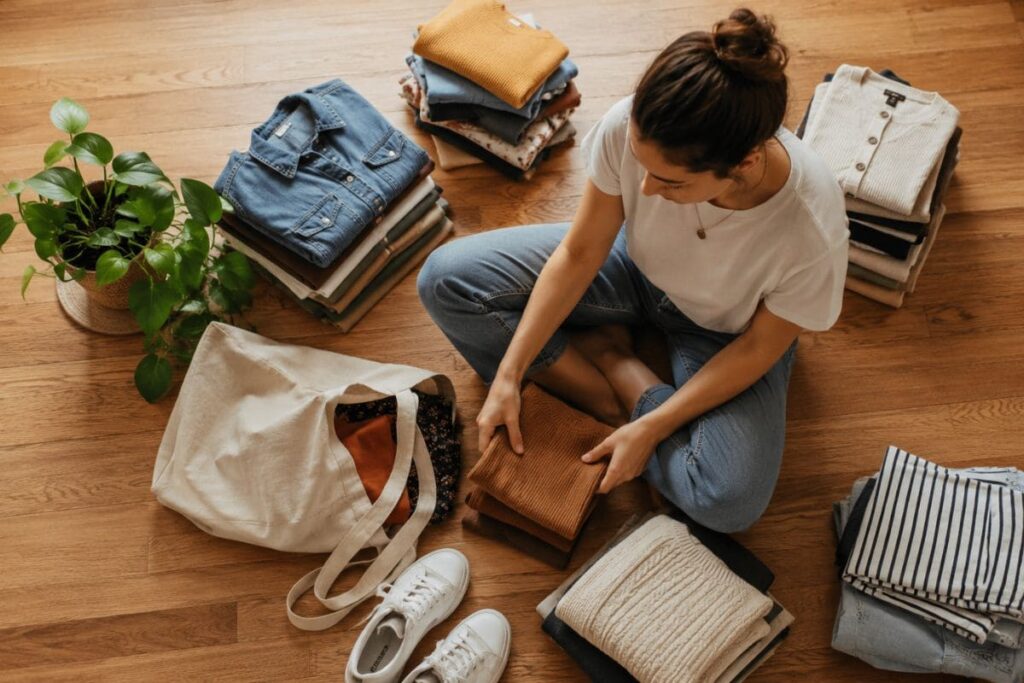 How to start a sustainable wardrobe on a budget – woman sorting secondhand clothes at home